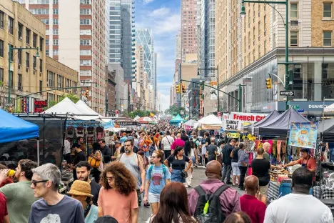 A high-angle view of a busy city street filled with people walking through an outdoor market with white tents.