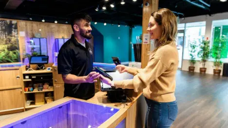 A friendly staff member behind a wooden counter assisting a customer in a modern, well-lit dispensary.