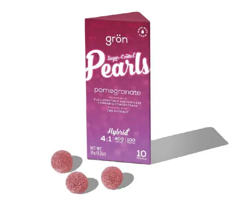A tall purple box of Grön Pomegranate Pearls edibles with three sugar-coated gummies resting on a white surface.