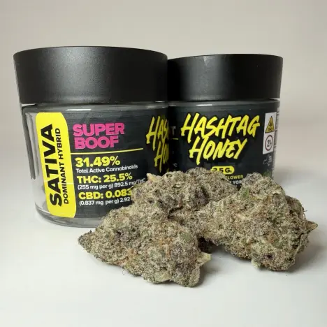 Two black jars of Hashtag Honey branded "Super Boof" Sativa flower next to several large, dense cannabis buds.