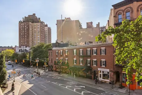 A sunlit street view of traditional brick brownstone buildings in a quiet urban neighborhood.
