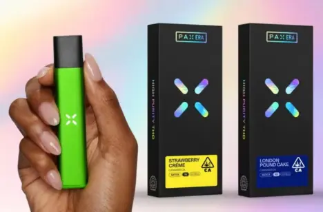 A hand holding a lime green PAX vape battery next to two black retail boxes for PAX Era pods.