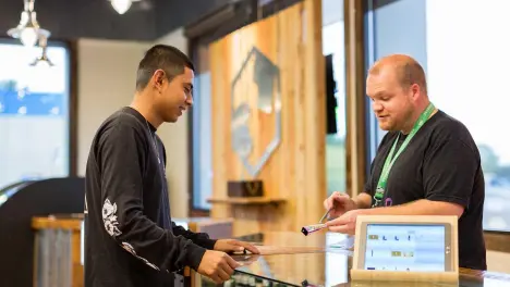 A retail employee assisting a customer at a digital checkout counter inside a modern shop.