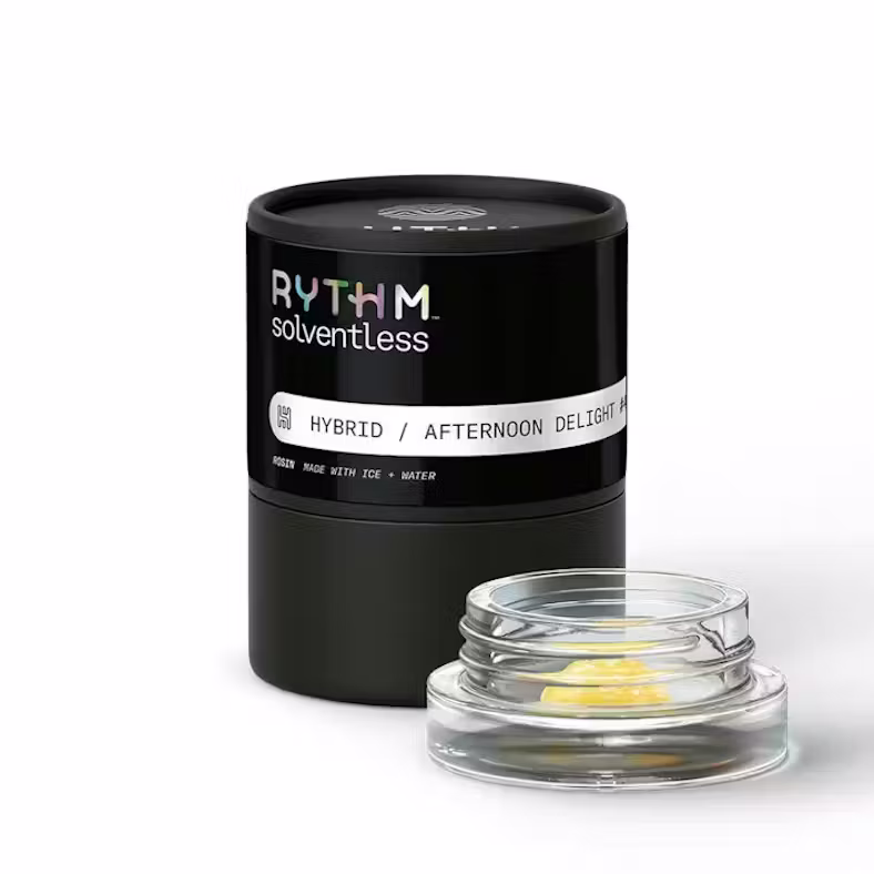 A small clear glass jar containing wax material, next to a black cylindrical case with "Rythm" text on a light grey surface.